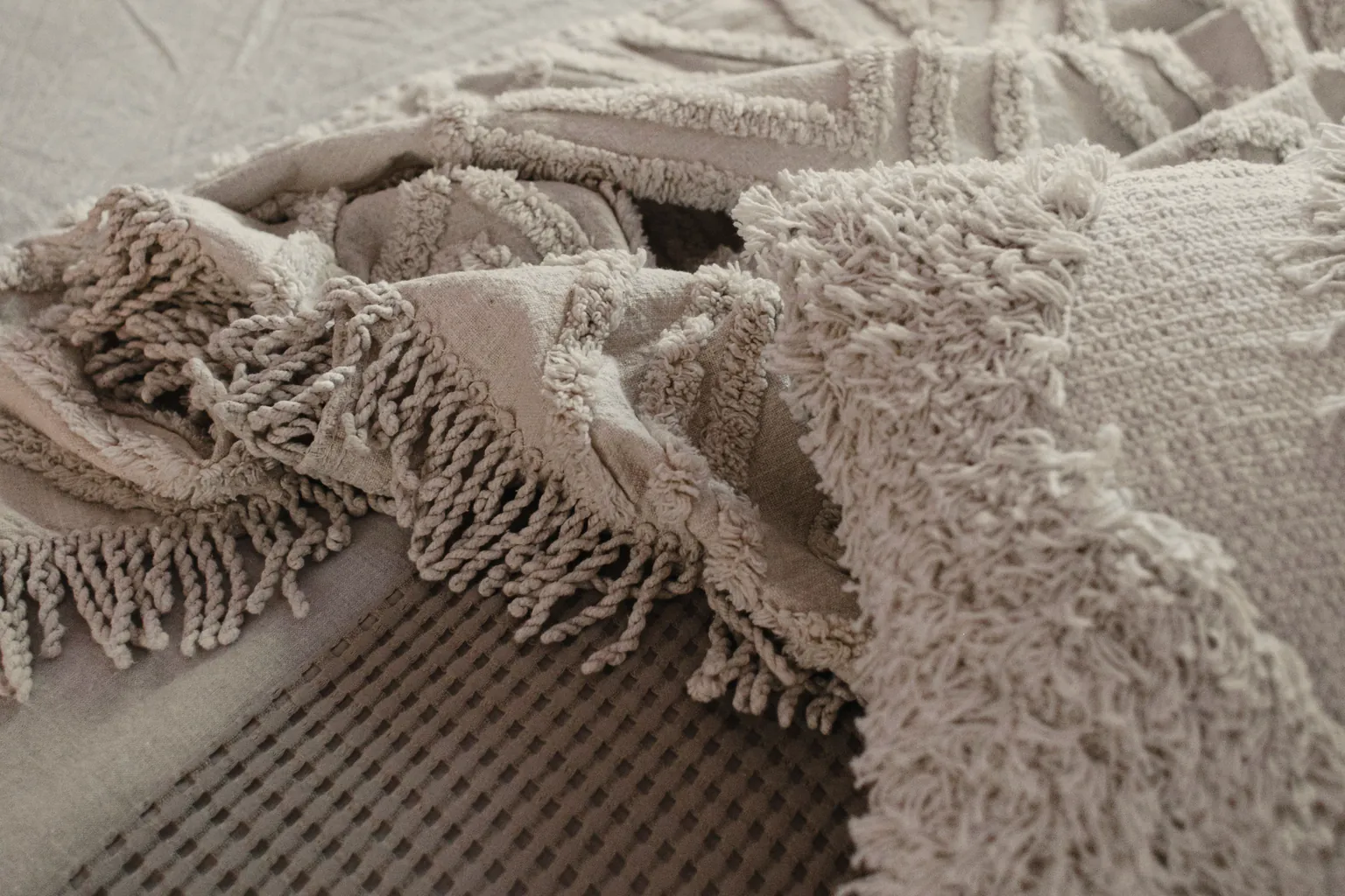 A cream knitted blanket over white and oatmeal linen at the corner of the bed