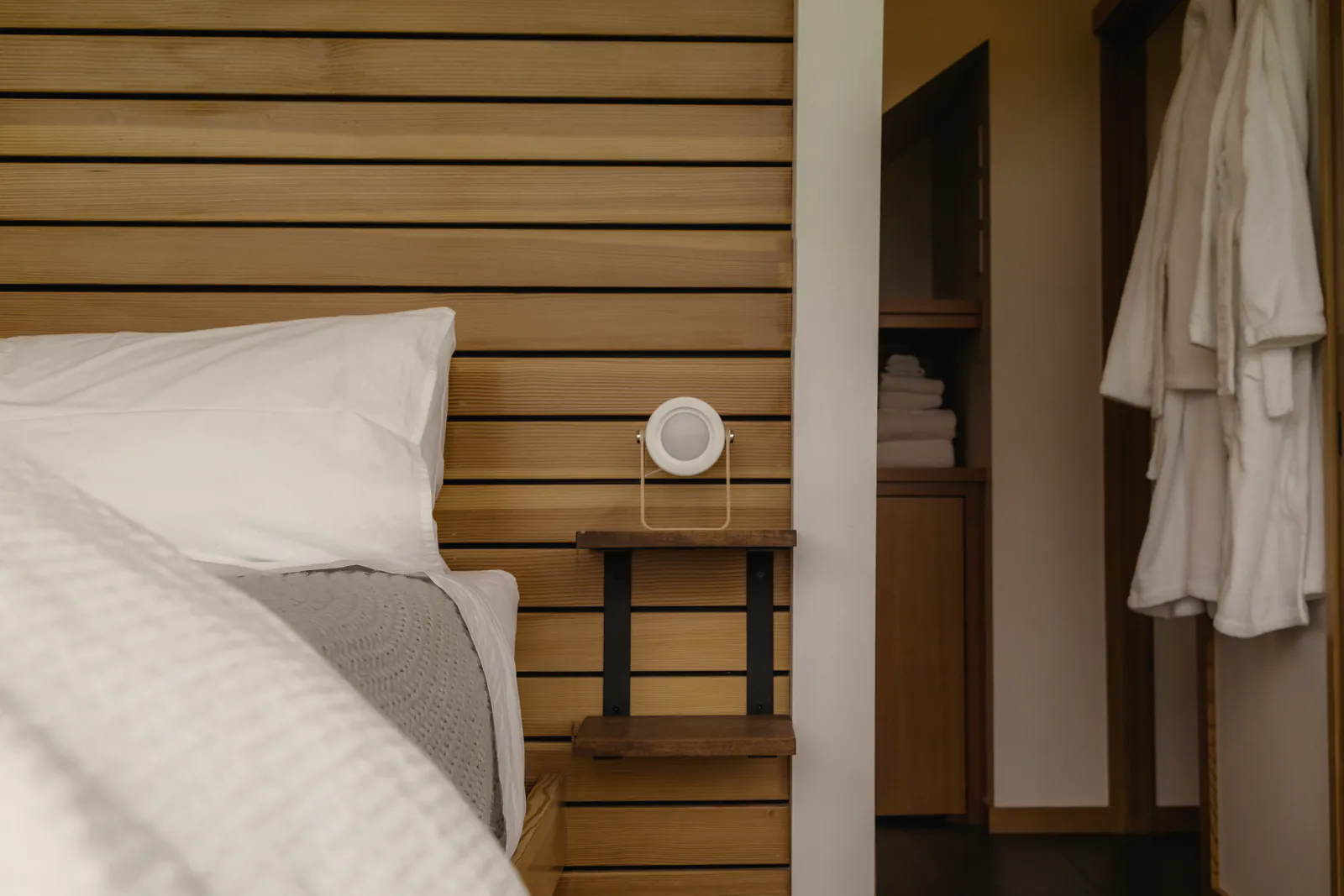A white pillow under the slatted timber bedhead, a lamp on its shelf and the door to the shower room beyond