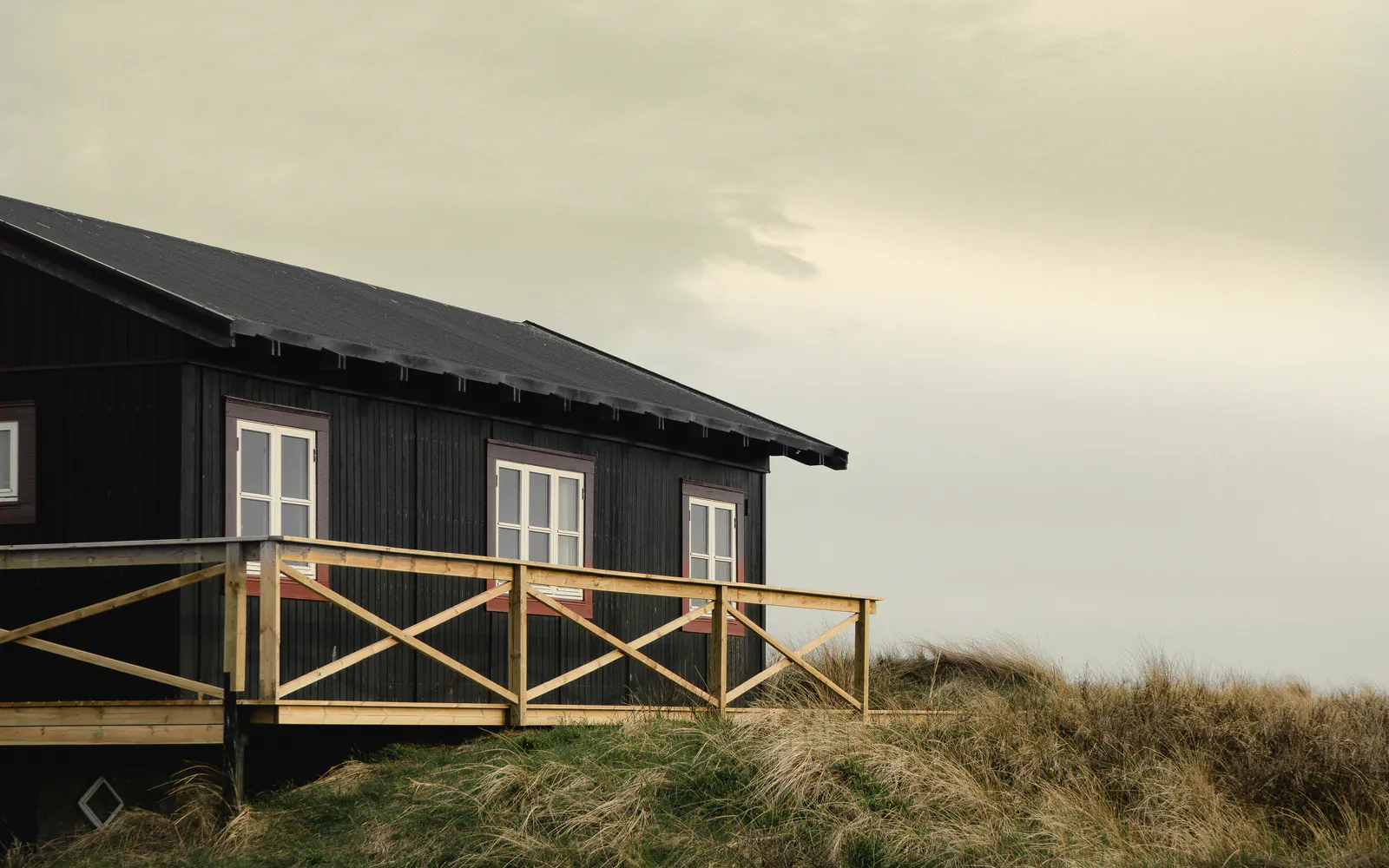 The house on its dune, its railed deck and door in a veiled late sun