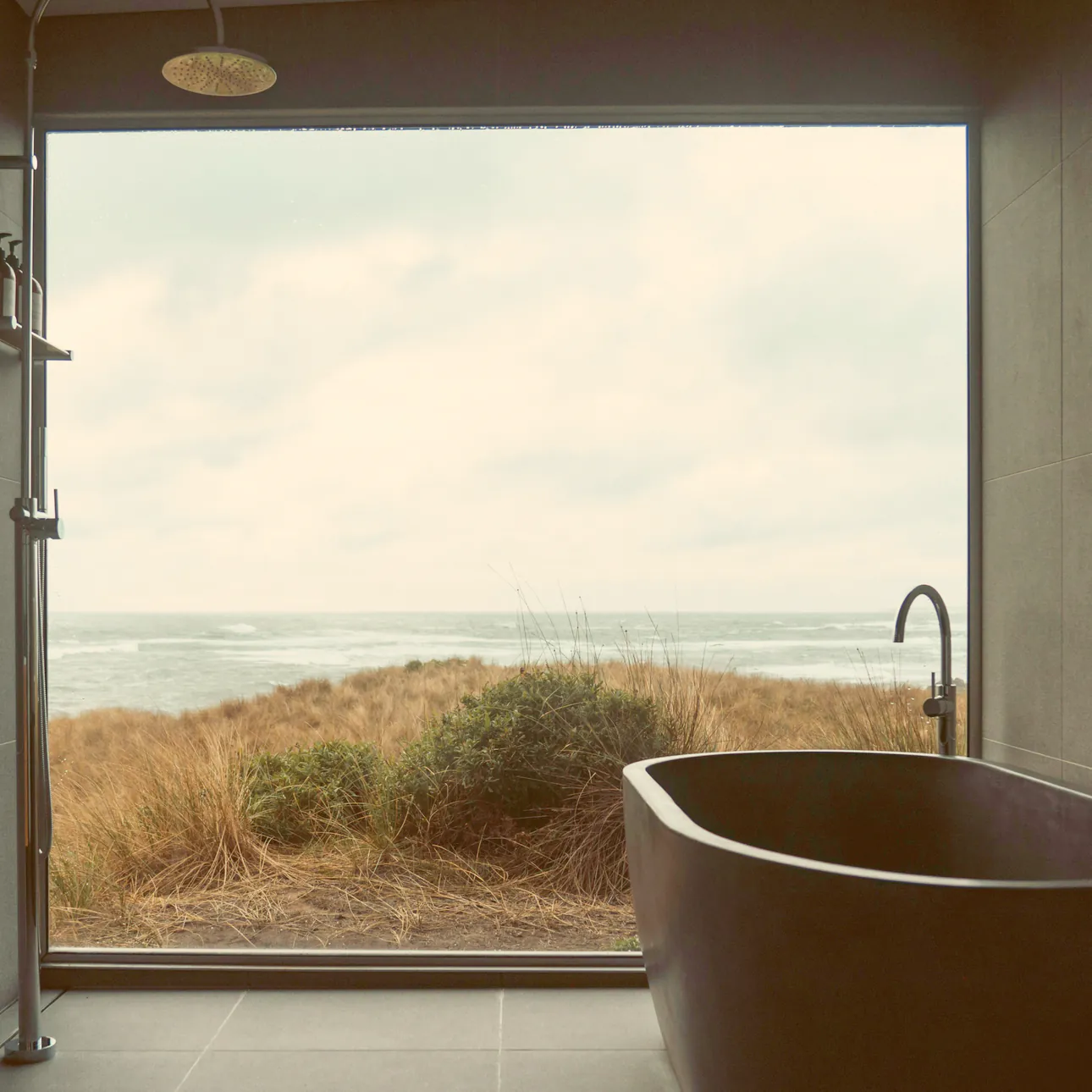 A deep stone bath under a picture window onto the dune grass and the sea