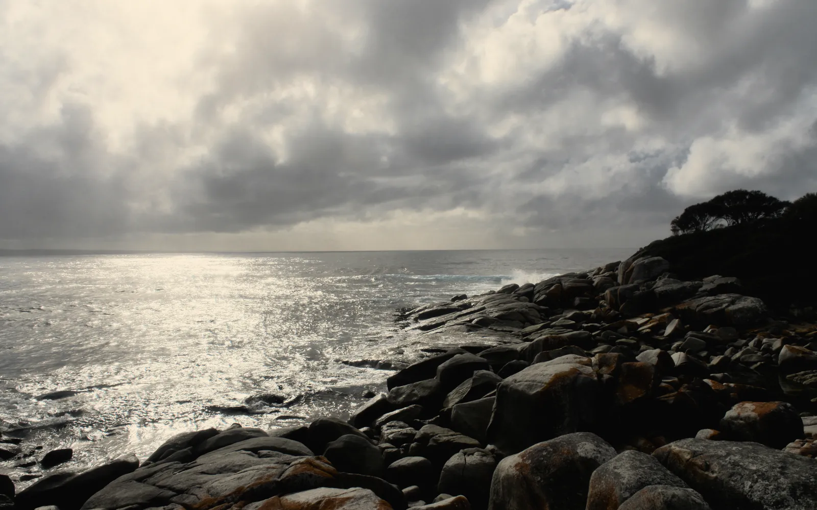 Lichen covered granite and white surf just off the shore, the sea silver under a veiled sun