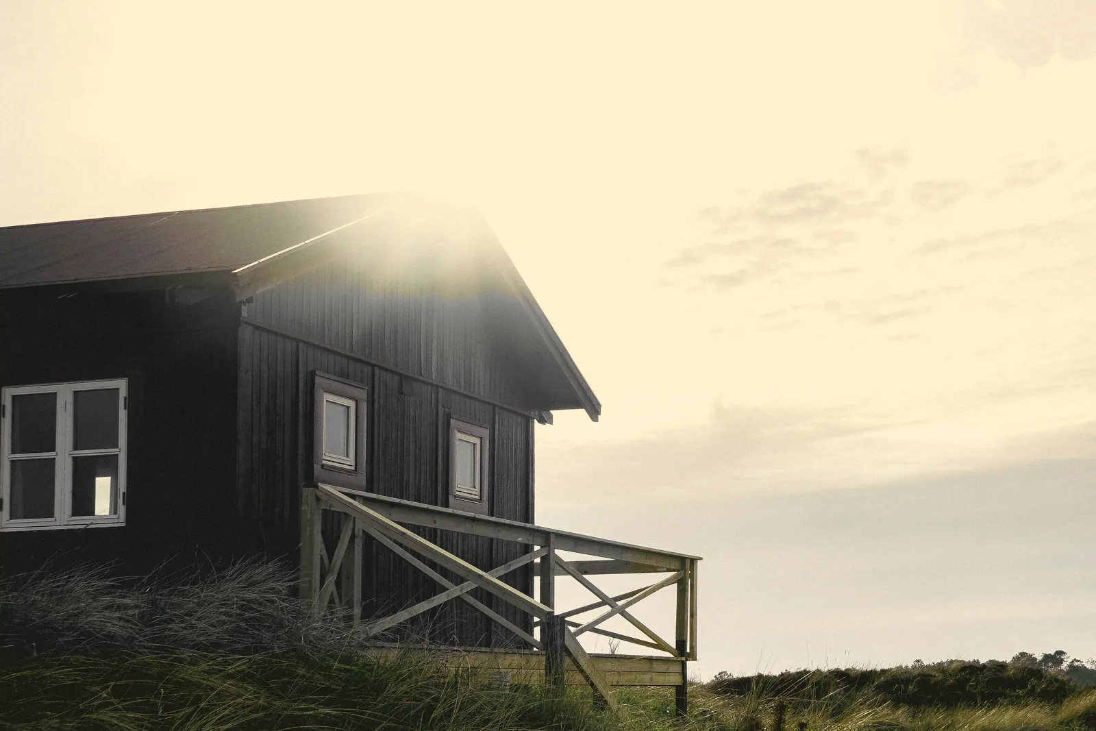 The corner of the house and its railed deck against a bright veiled sky, marram on the dune in front