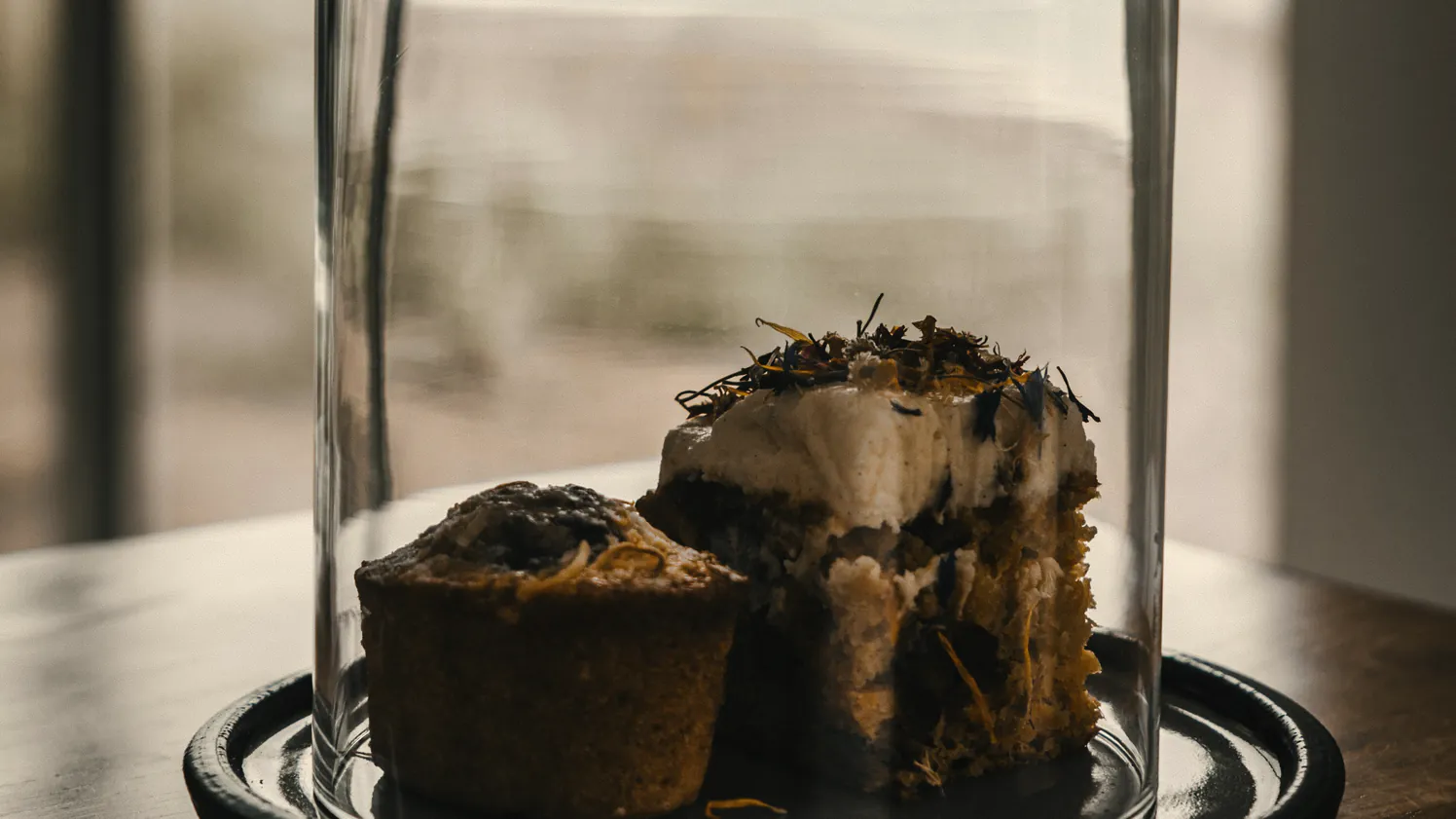 A cake under a glass dome on the timber table, the beach pale through the window behind