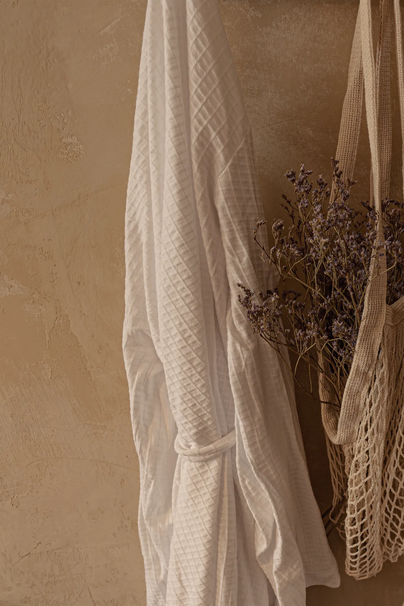 A white waffle robe on a hook against a warm plaster wall in soft side light