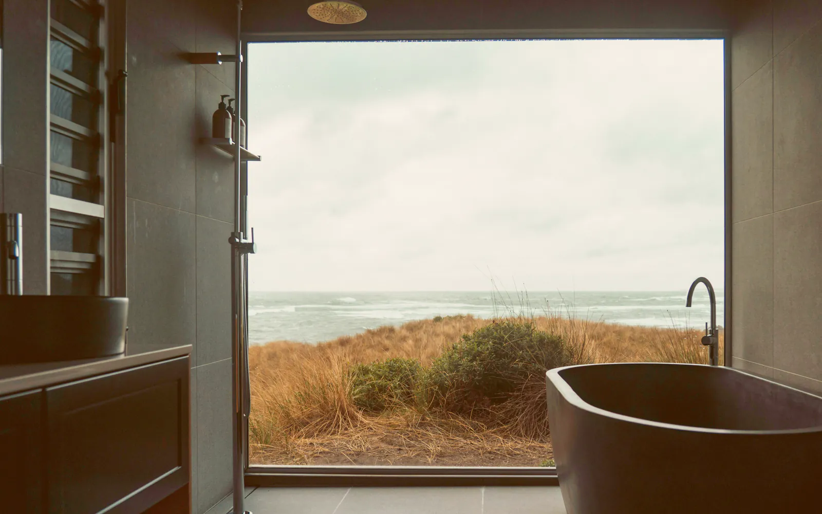 A deep stone bath under a picture window onto the dune grass and the sea