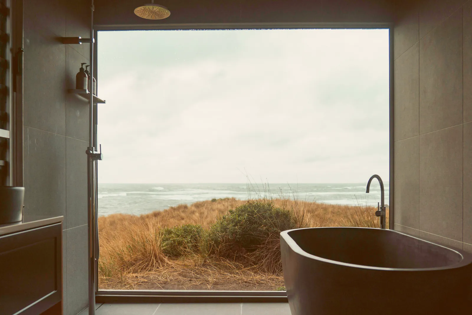 A deep stone bath under a picture window onto the dune grass and the sea