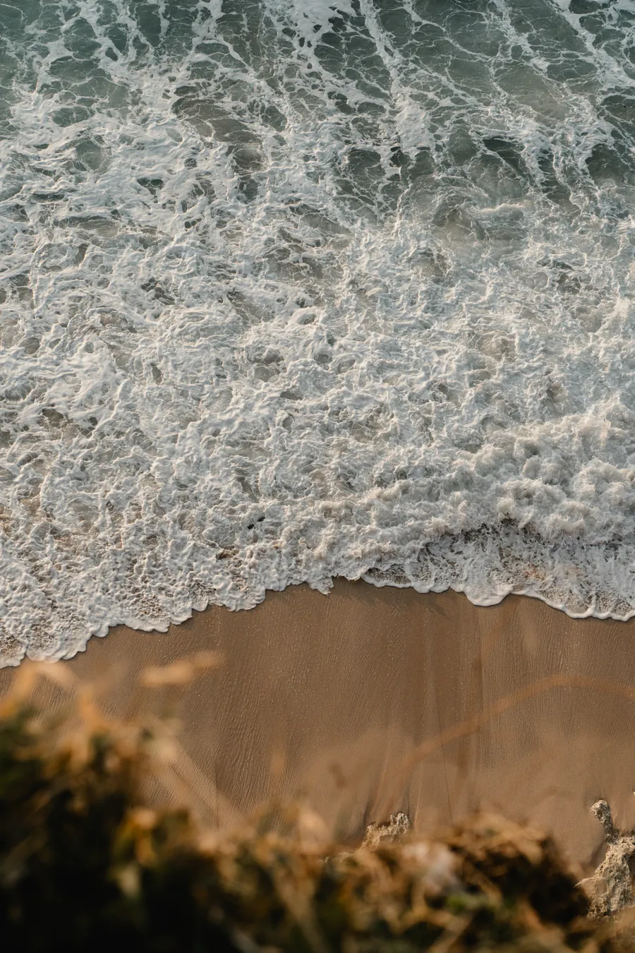 The beach below the room from above, foam running in over the sand