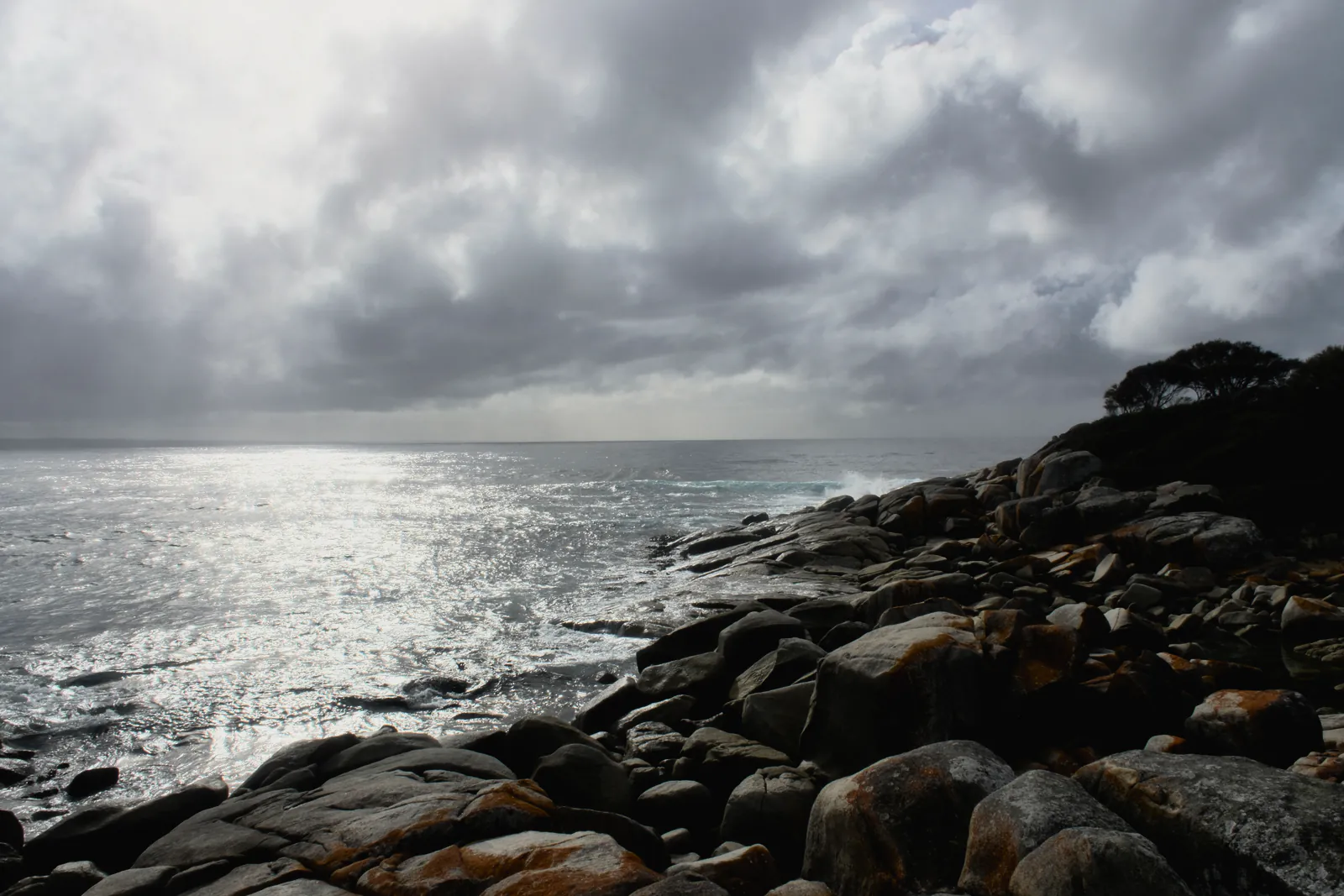 Lichen covered granite and white surf just off the shore, the sea silver under a veiled sun
