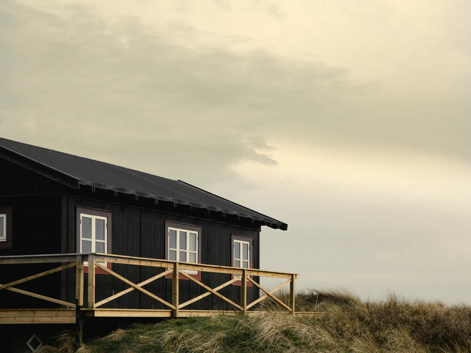 The house on its dune, its railed deck and door in a veiled late sun