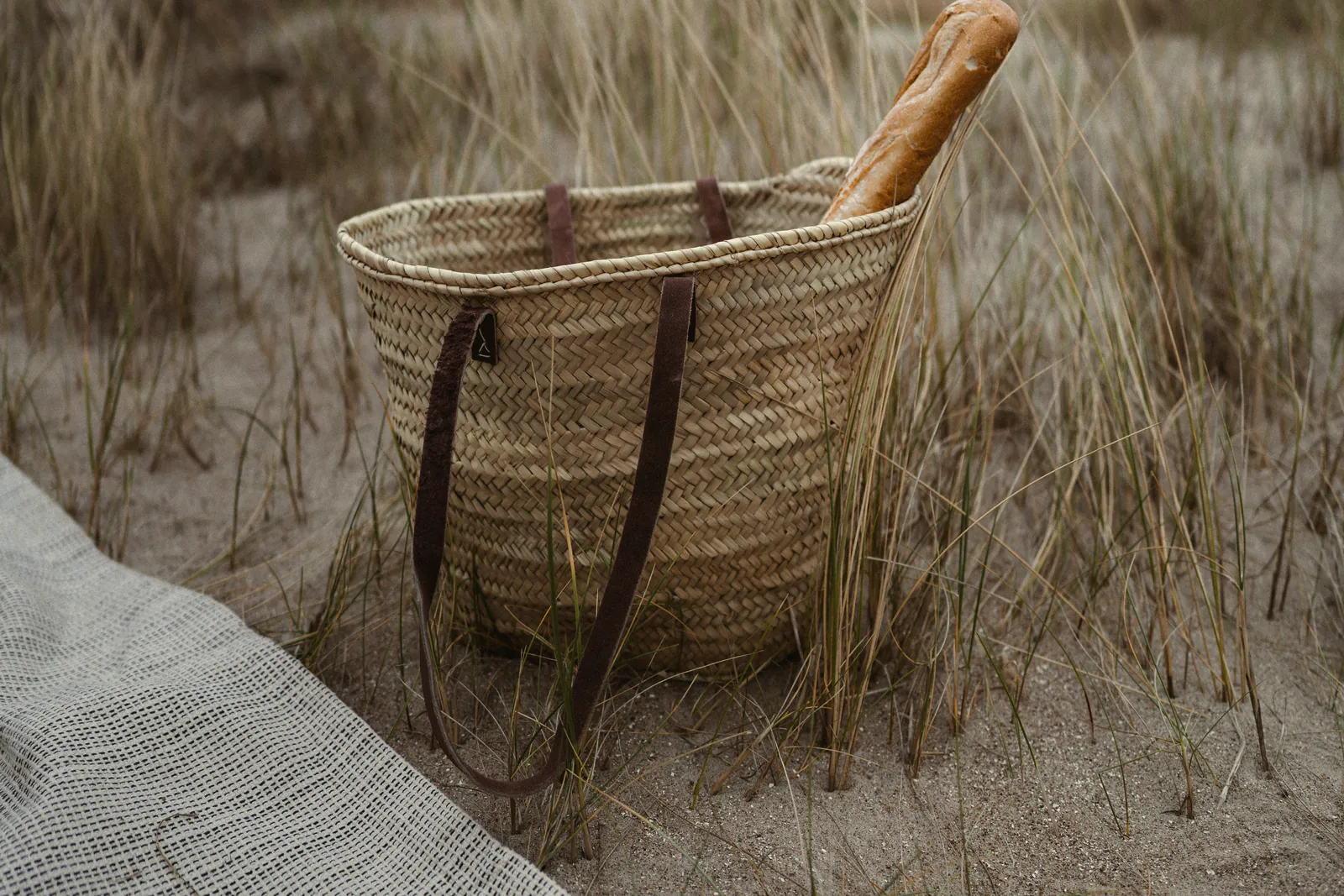 A woven basket with a loaf of bread in the marram, a linen blanket in front