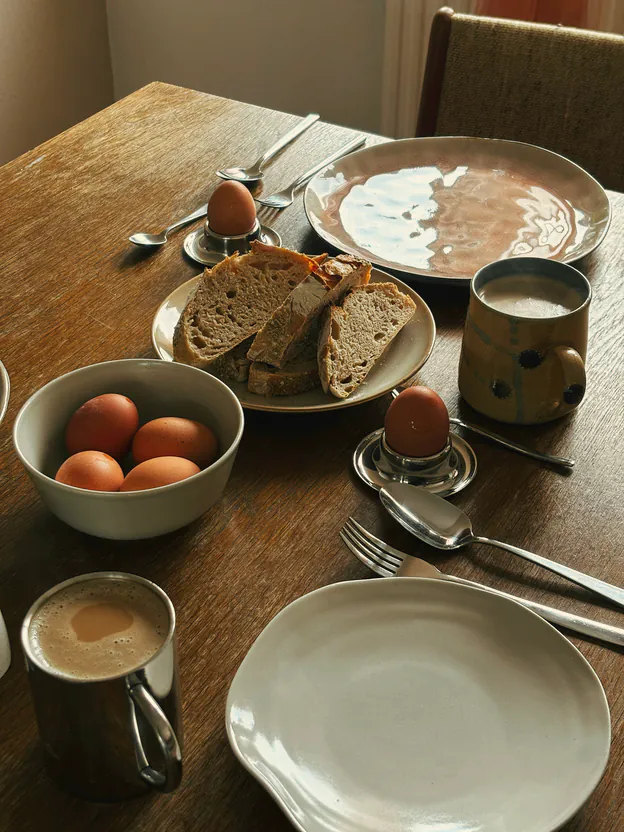 Eggs in cups and in a bowl, sourdough, coffee and stoneware plates on the dark timber table