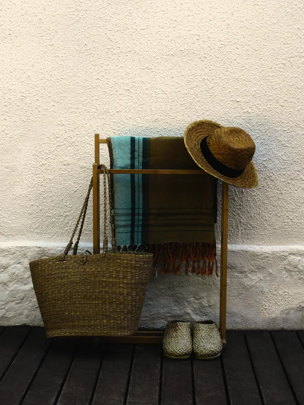 Striped beach towels on a timber rail, a woven basket, a straw hat and canvas shoes on the boards